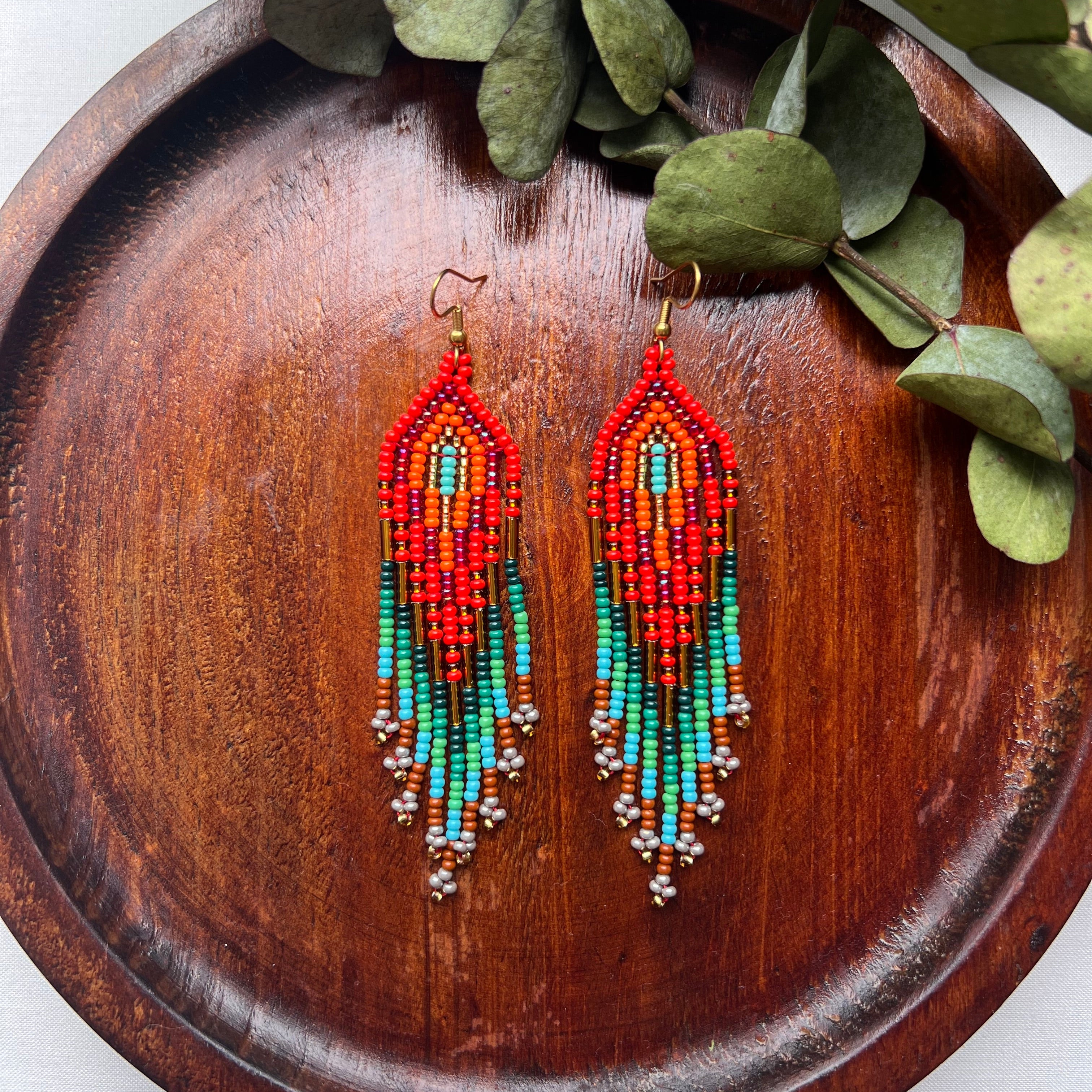 Colorful beaded earrings on a wooden tray with green leaves.