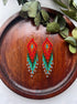 Colorful beaded earrings on a wooden tray with green leaves.