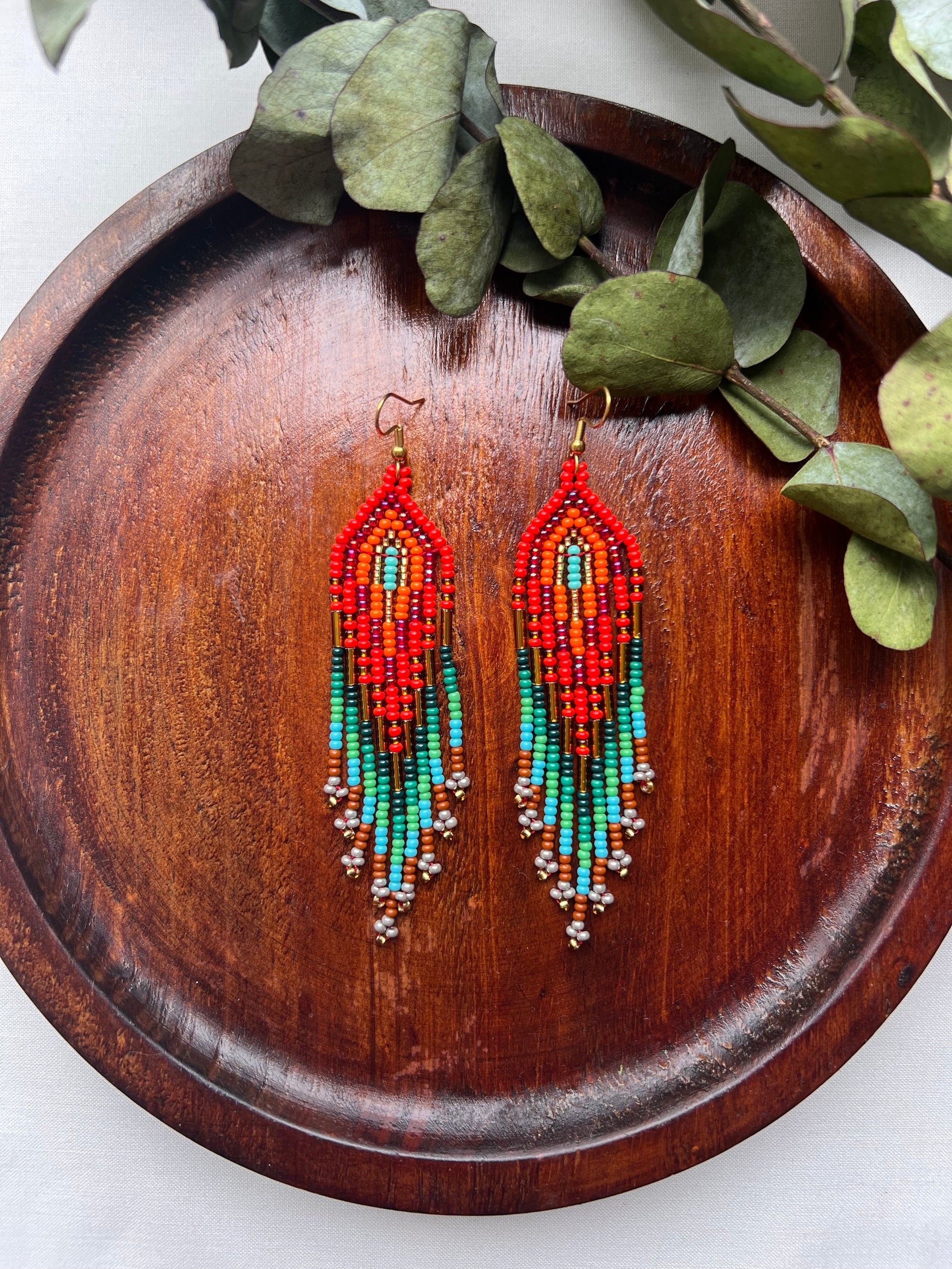 Colorful beaded earrings on a wooden tray with green leaves.